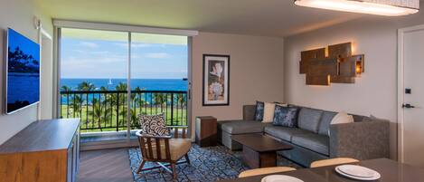 A modern living room with a balcony overlooking a beach, a dining area with plates, and a mounted artwork.