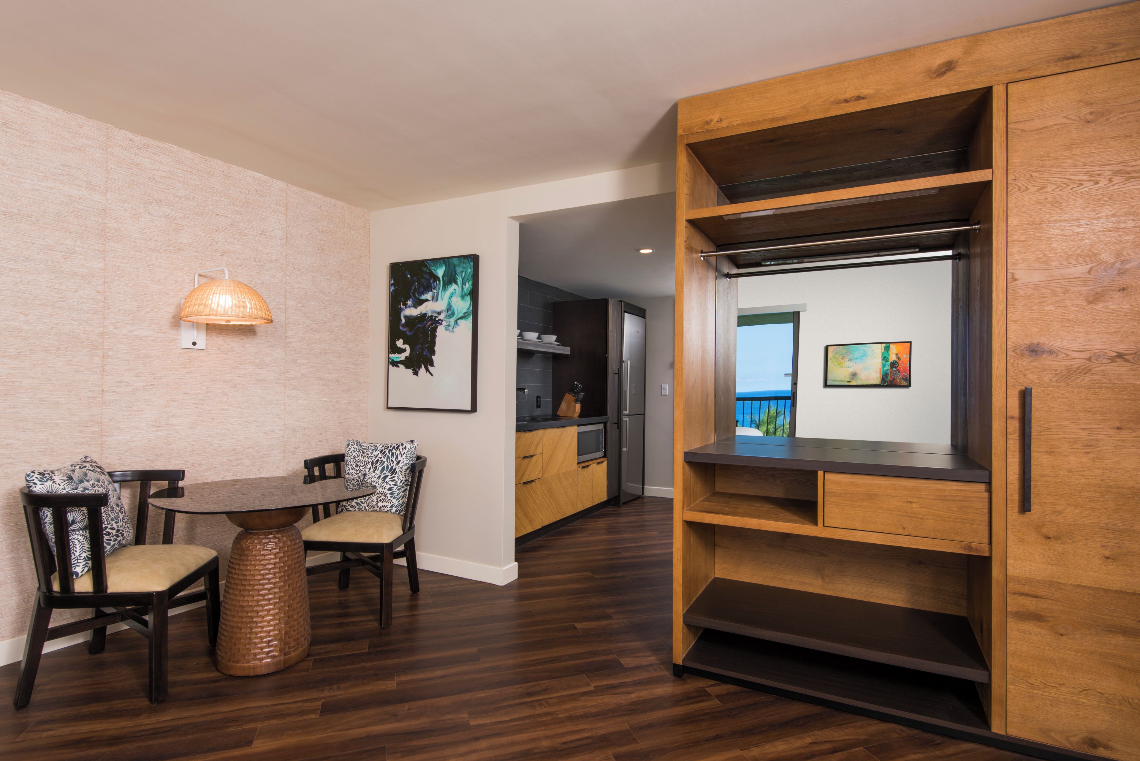 A modern kitchen with wooden cabinets, a dining area with a table and chairs, and artwork on the walls.