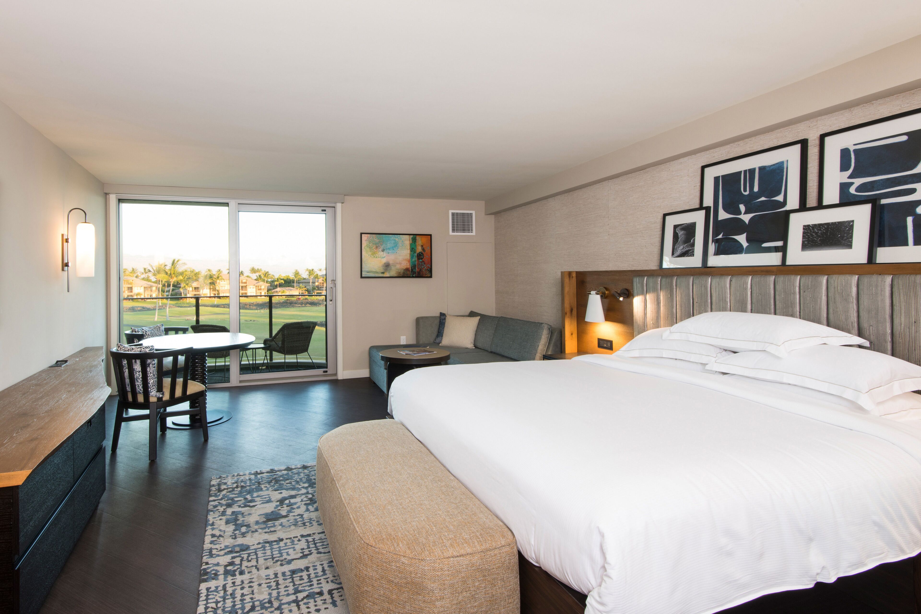 Une chambre d’hôtel moderne dotée d’un grand lit, d’un coin repas avec une table et des chaises, d’un canapé et offrant une vue sur un terrain de golf grâce aux portes coulissantes.