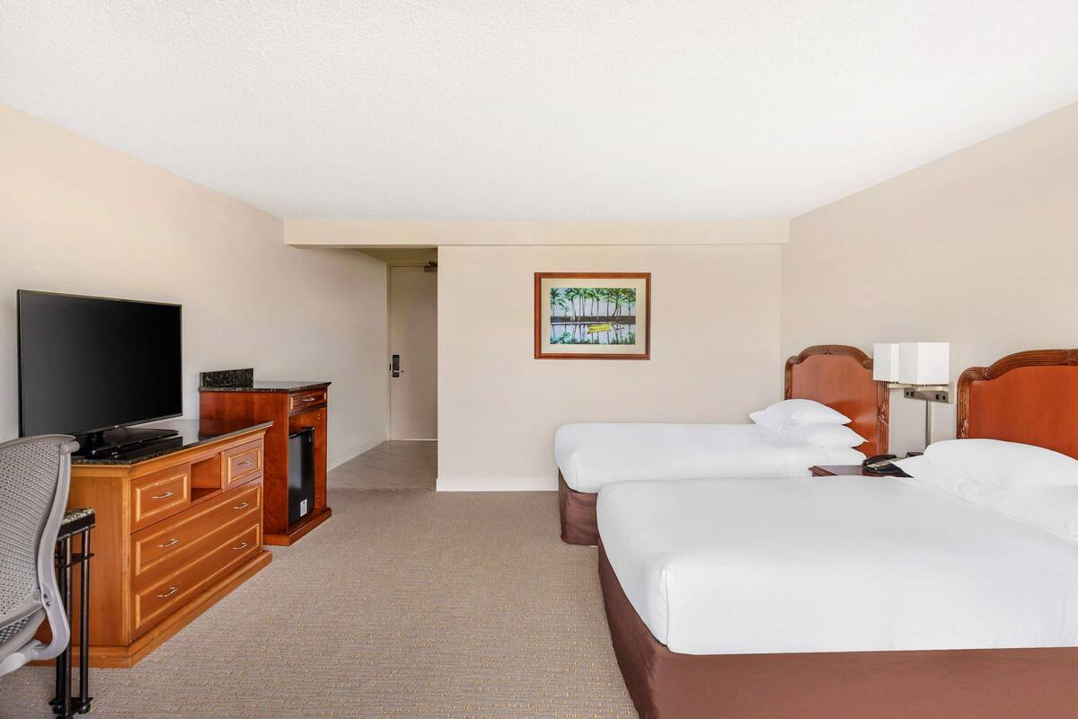 Une chambre d’hôtel avec un lit, un bureau avec une télévision, une commode et un tableau au mur.