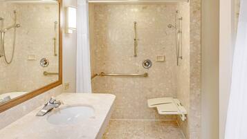 A bathroom with a sink, mirror, shower, and grab bars.