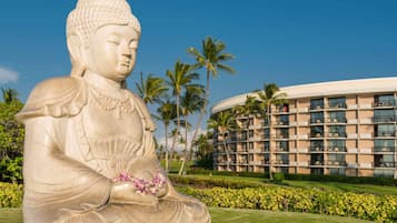 Una gran estatua de Buda en una zona ajardinada, con un edificio de hotel al fondo.