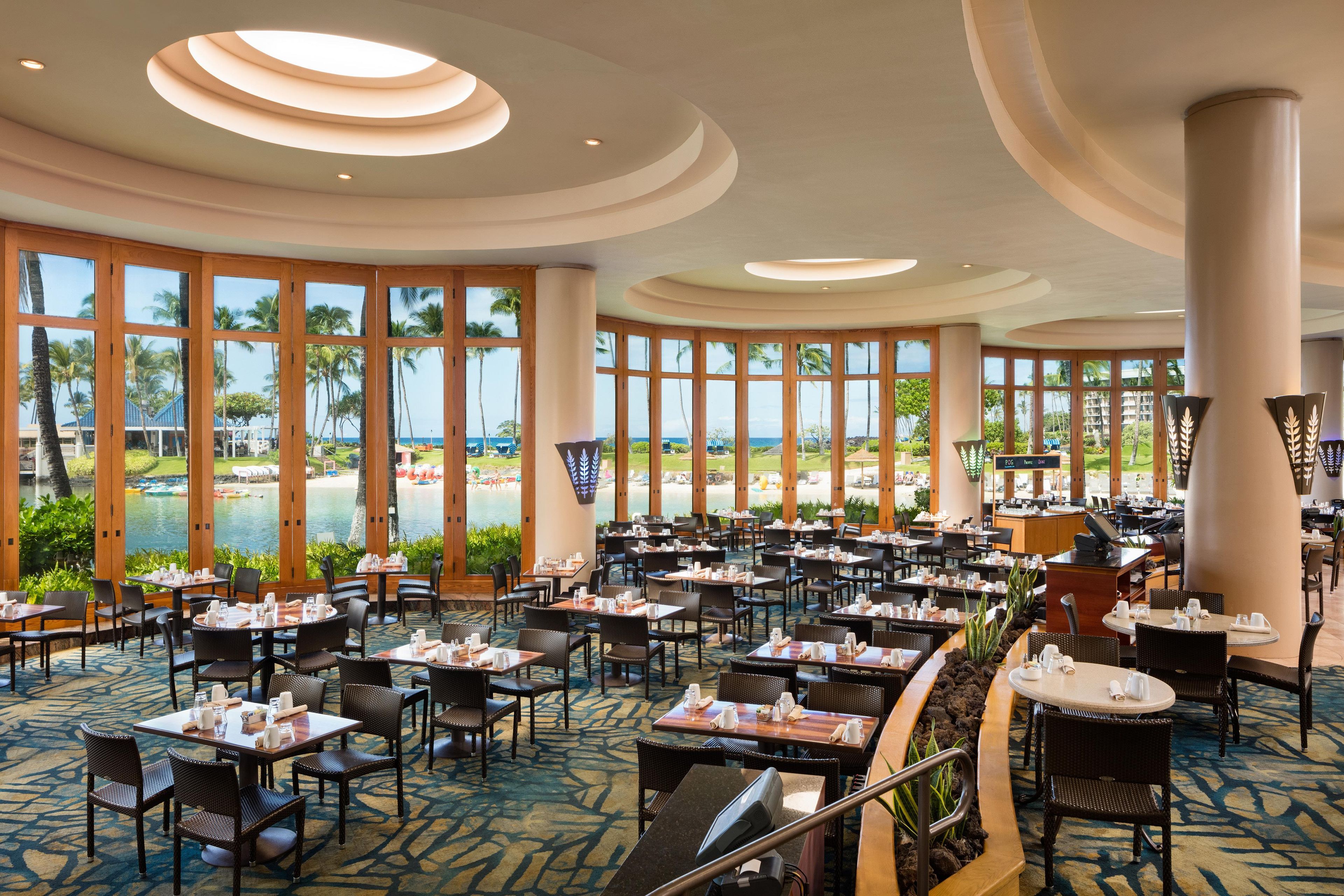 A spacious indoor dining area with large windows offering a view of a beach and pool.