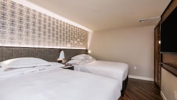 Une chambre d’hôtel avec deux lits, une tête de lit ornée d’un motif floral, une table de chevet avec une lampe et une armoire.