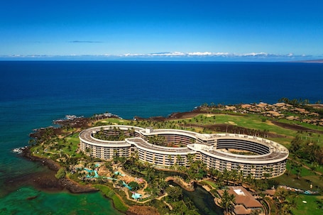 A large, circular hotel with multiple floors, surrounded by lush greenery and a pool area.