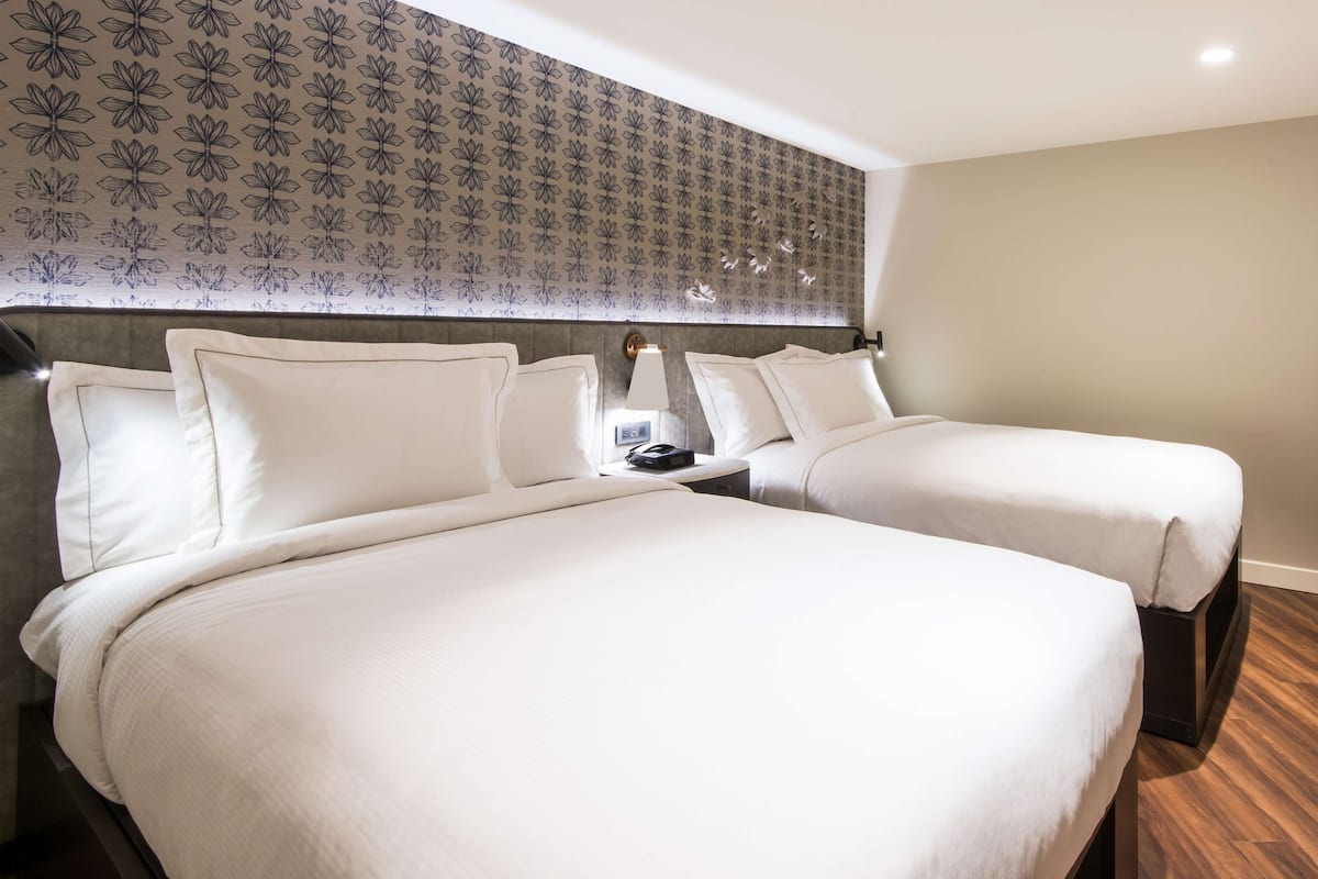 Une chambre d’hôtel avec deux lits, un papier peint à motifs et une tête de lit moderne.