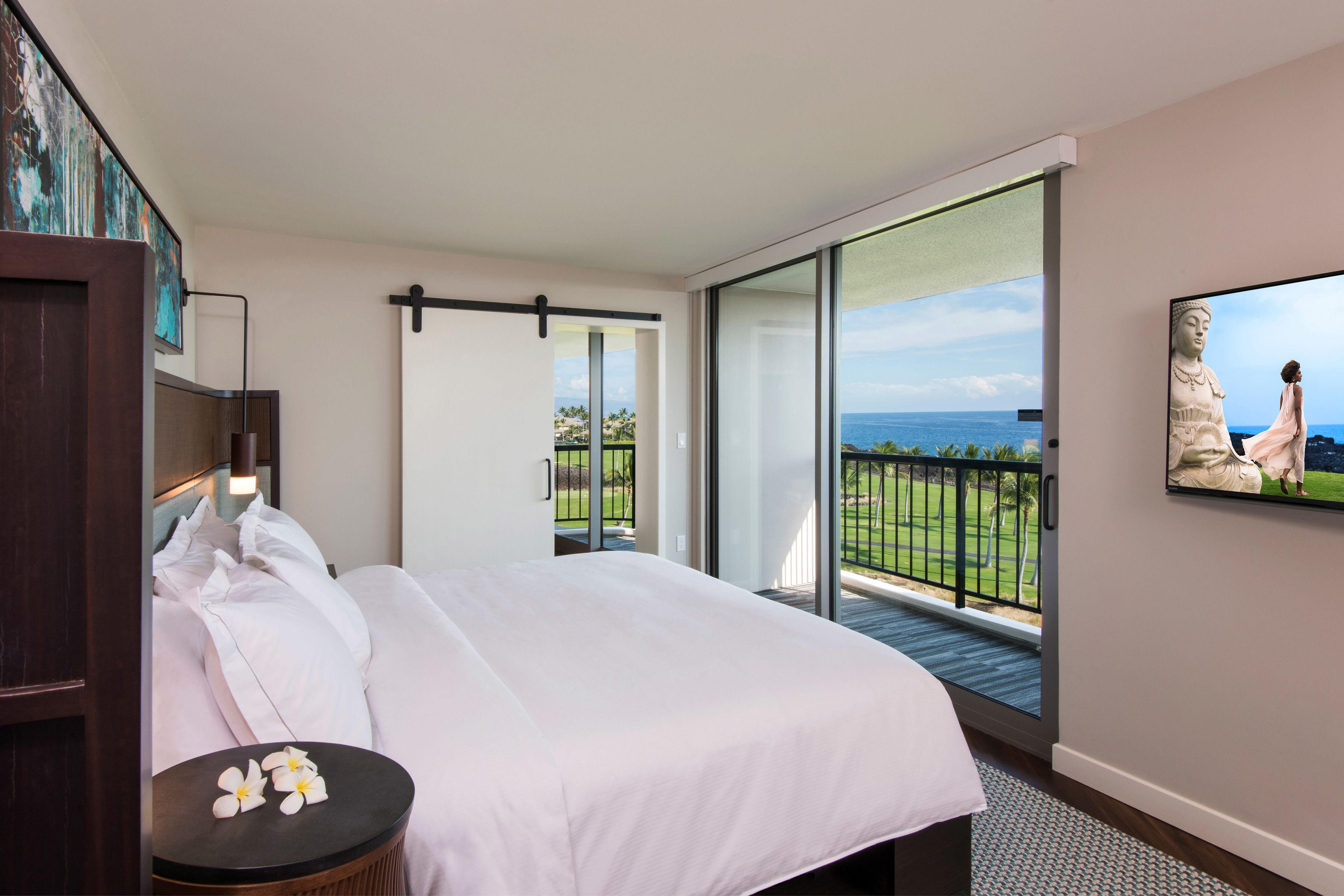 Camera d'albergo con un letto grande, un tavolino con fiori, un quadro e un balcone vista mare.