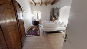 Una habitación con un armario de madera, una cama con ropa de cama blanca, un tapete estampado y una pared de piedra.