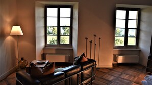 Una habitación con sofá de cuero, una lámpara de pie y dos ventanas con vistas a zonas verdes.