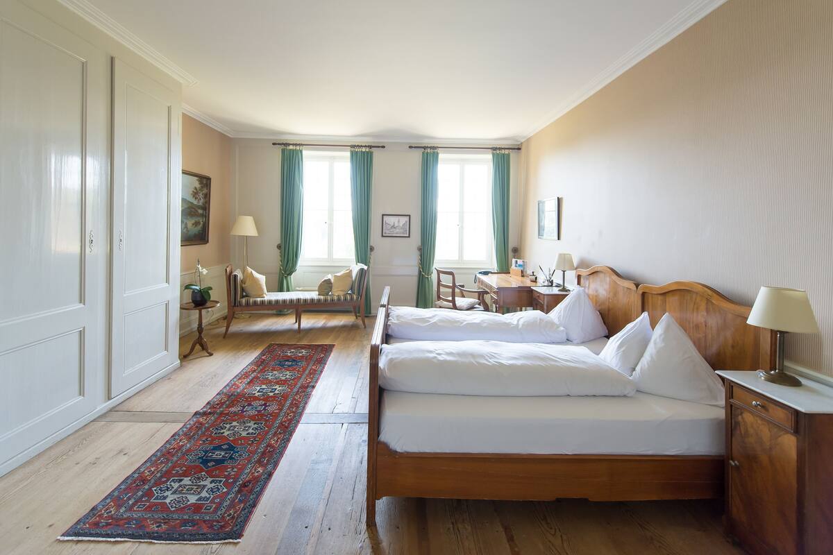 A hotel room with two beds, a desk, a chair, a small table, and a window with curtains.