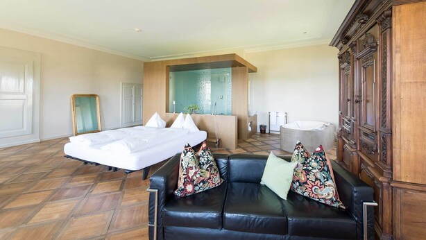 Amplia habitación de hotel con una cama grande, un sofá, un armario de madera y una bañera.