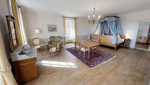 Un dormitorio con cama con dosel, una mesa de comedor con sillas, una mesita de noche con lámpara y un espejo grande.