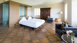 Una habitación de hotel amplia con una cama grande, un sofá, un armario de madera y una mesa de centro de vidrio.