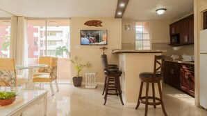 A modern kitchen with a flat-screen TV, wooden bar stools, and a dining area with a glass table and chairs. - Ocho Rios Vacation - Apartment (Ocho Rios)