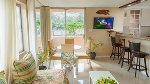 A modern living room with a sofa, a dining table, and chairs. A flat-screen TV is mounted on the wall. - Ocho Rios Vacation - Apartment (Ocho Rios)
