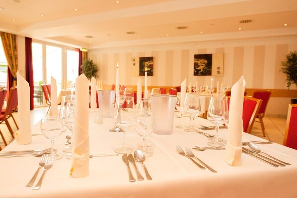 A dining table set with white tablecloth, candles, and glassware in a well-lit room with striped walls and red chairs. - Hotel Schützenburg (Burscheid)
