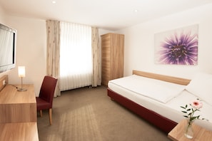 A hotel room with a bed, a desk, a chair, a wardrobe, and a painting on the wall. - Hotel Schützenburg (Burscheid)