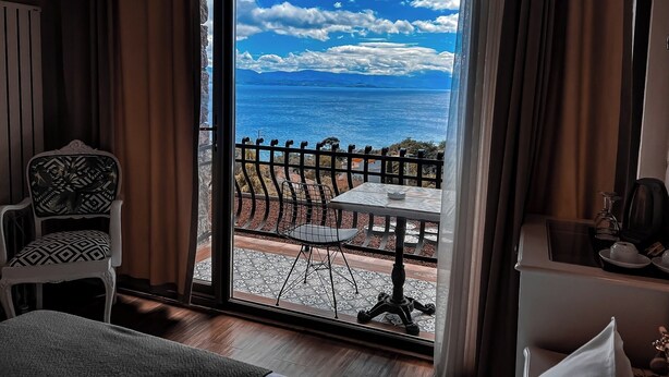 A room with a large window overlooking a scenic view of the sea and mountains.