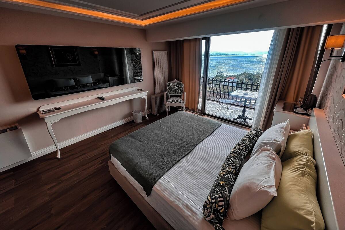 Ein modernes Hotelzimmer mit einem großen Bett, einem wandmontierten Flachbildfernseher, einem Balkon mit Meerblick und einem kleinen Tisch mit einem Stuhl.