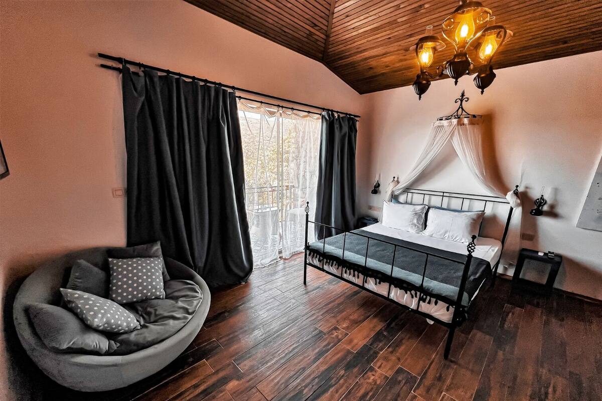 Ein Schlafzimmer mit einem Bett, einem Sessel, einem Himmelsbett, einer Kristallleuchtre und Blick durch das Fenster.