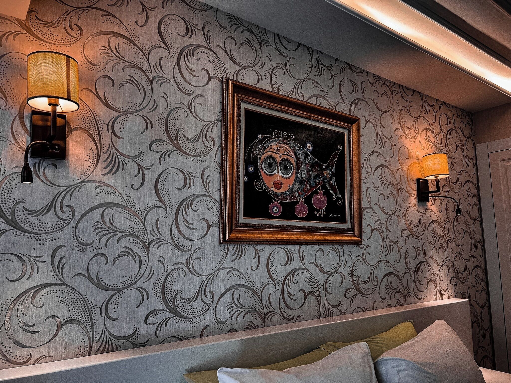 A bedroom with a patterned wallpaper, a framed artwork, and two wall-mounted lamps.