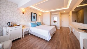 A hotel room with a bed, bedside tables, a desk, a chair, a wardrobe, a mirror, and a door.