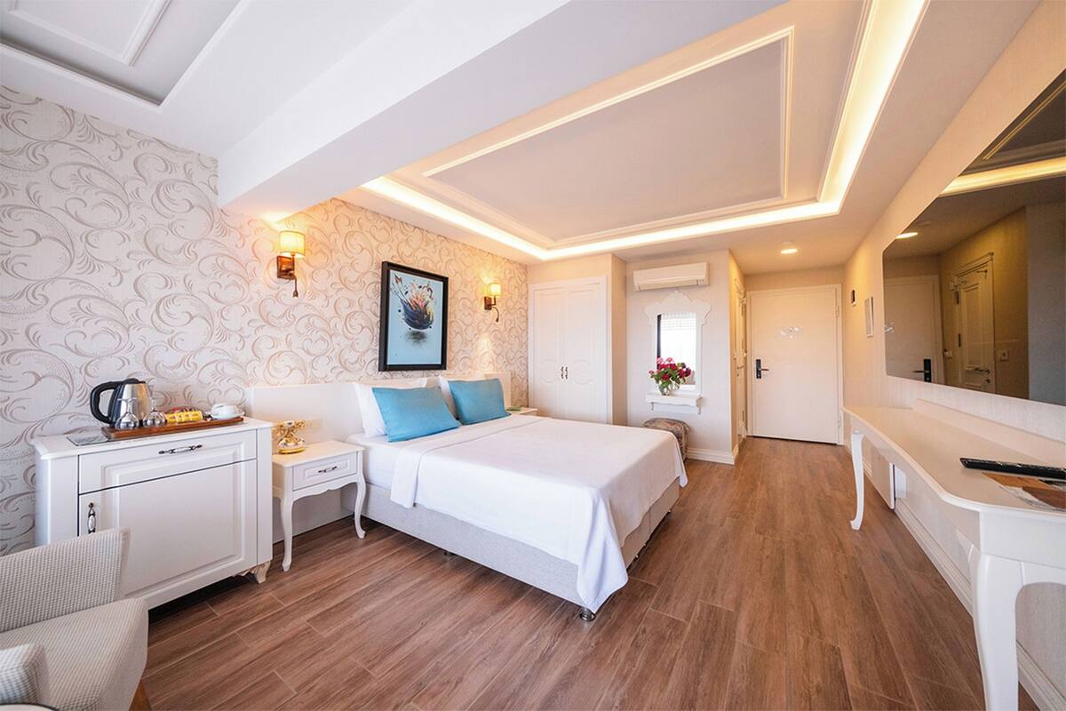 Ein Hotelzimmer mit Bett, Nachttischen, Schreibtisch, Stuhl, Kleiderschrank, Spiegel und Tür.