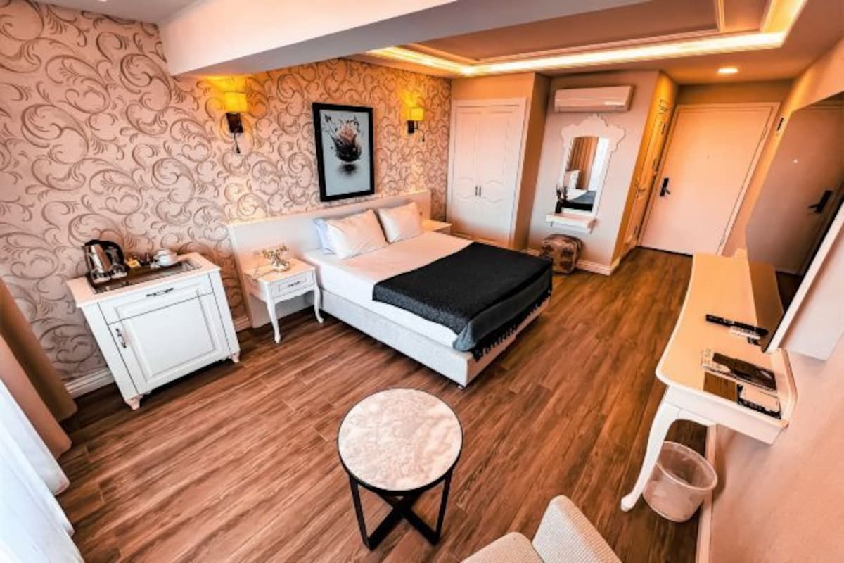 A bedroom with a bed, bedside tables, a desk, a chair, and a small stool.
