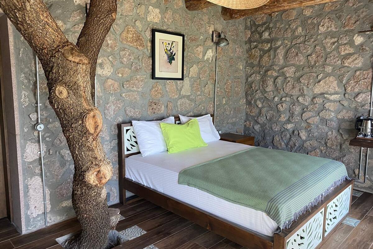 Ein Schlafzimmer mit einer Steinsäule, einem Bettgestell aus Holz, einem Baumstamm und einem botanischen Kunstdruck in einem Rahmen.