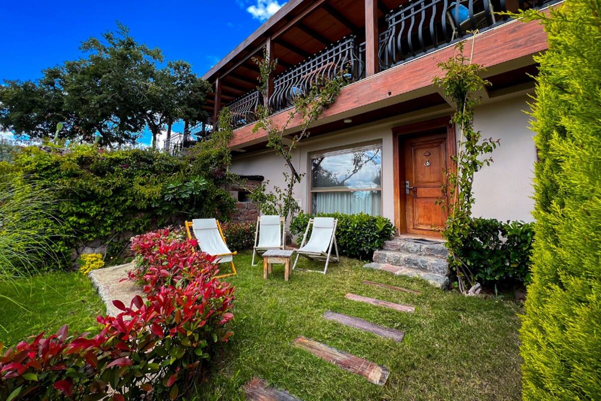 Ein zweistöckiges Haus mit Balkon, Holztür und Garten mit Stühlen und trittfesten Steinen.