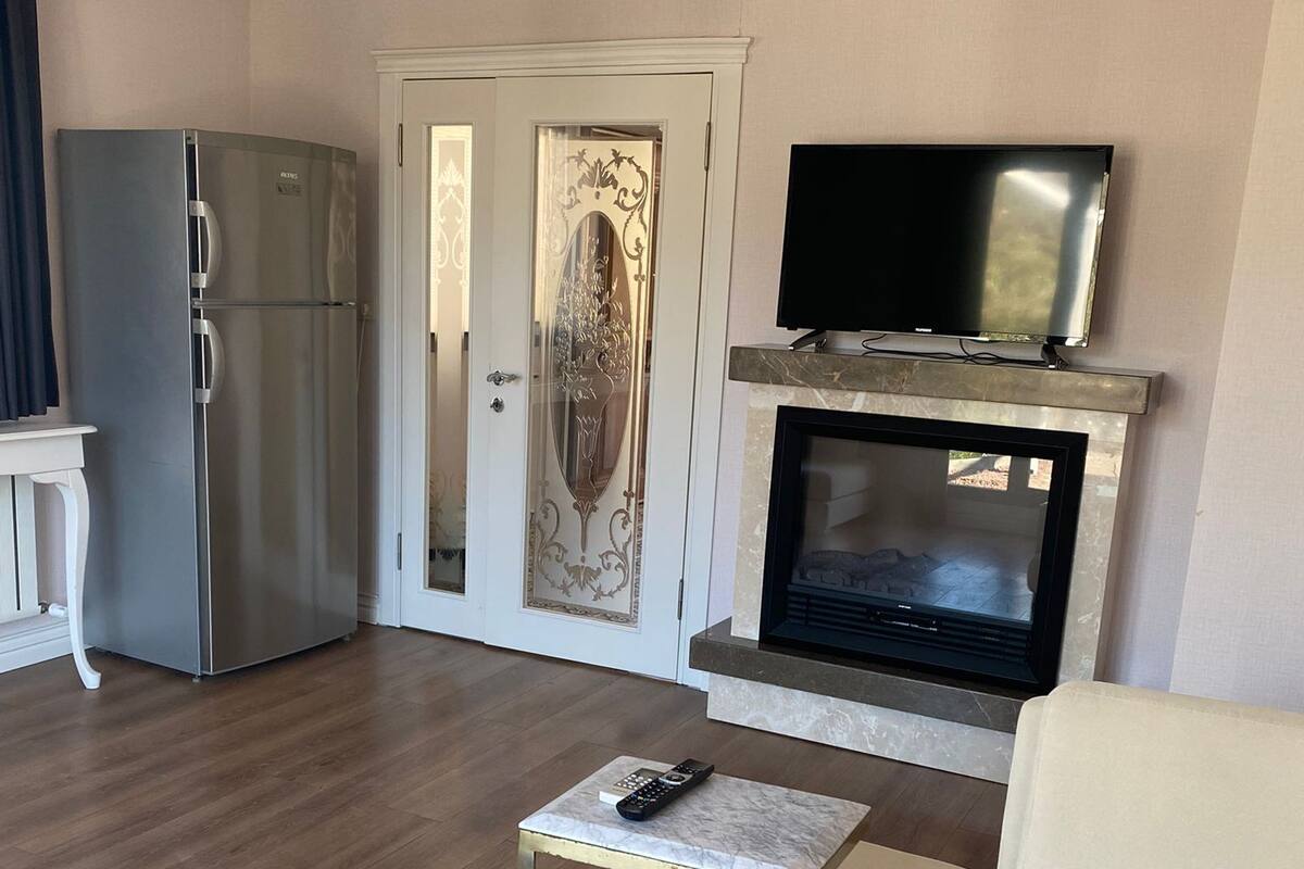 Ein Wohnzimmer mit einer Couch, einem Couchtisch, einem Fernseher, einem Kamin und einer Küchenzeile mit einem Kühlschrank.