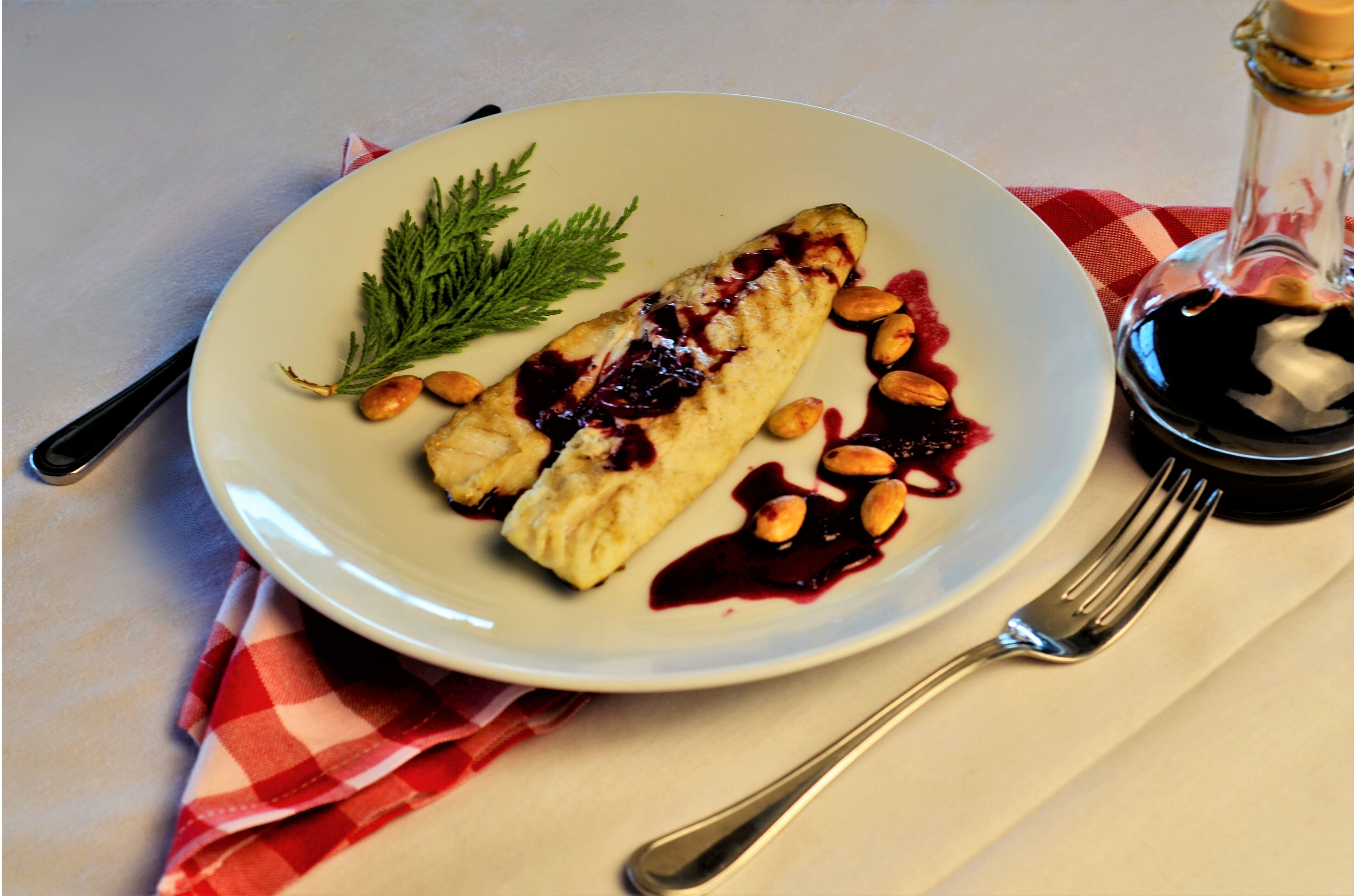 Un piatto con un fagottino di pasta sfoglia, noci e salsa ai frutti di bosco, accompagnati da una forchetta e una bottiglia di salsa.