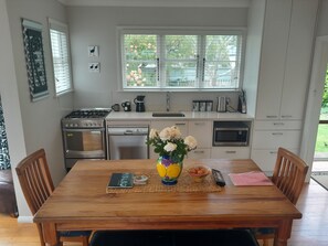 A modern kitchen with white cabinets, a stainless steel stove, and a dishwasher. There is a dining table with chairs, a vase of flowers, and a bowl of eggs.