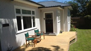Ein Haus mit einer Holzterrasse, einer kleinen Terrasse mit Stühlen und einem gepflegten Rasen.
