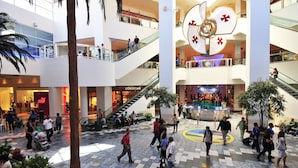 Un centro comercial de varios niveles con escaleras mecánicas, palmeras y un elemento decorativo central.