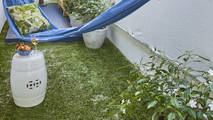 Una hamaca, una mesita con una bebida y plantas en macetas en un jardín.