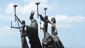 Una estatua de tres figuras sobre un pedestal de piedra junto al muelle.