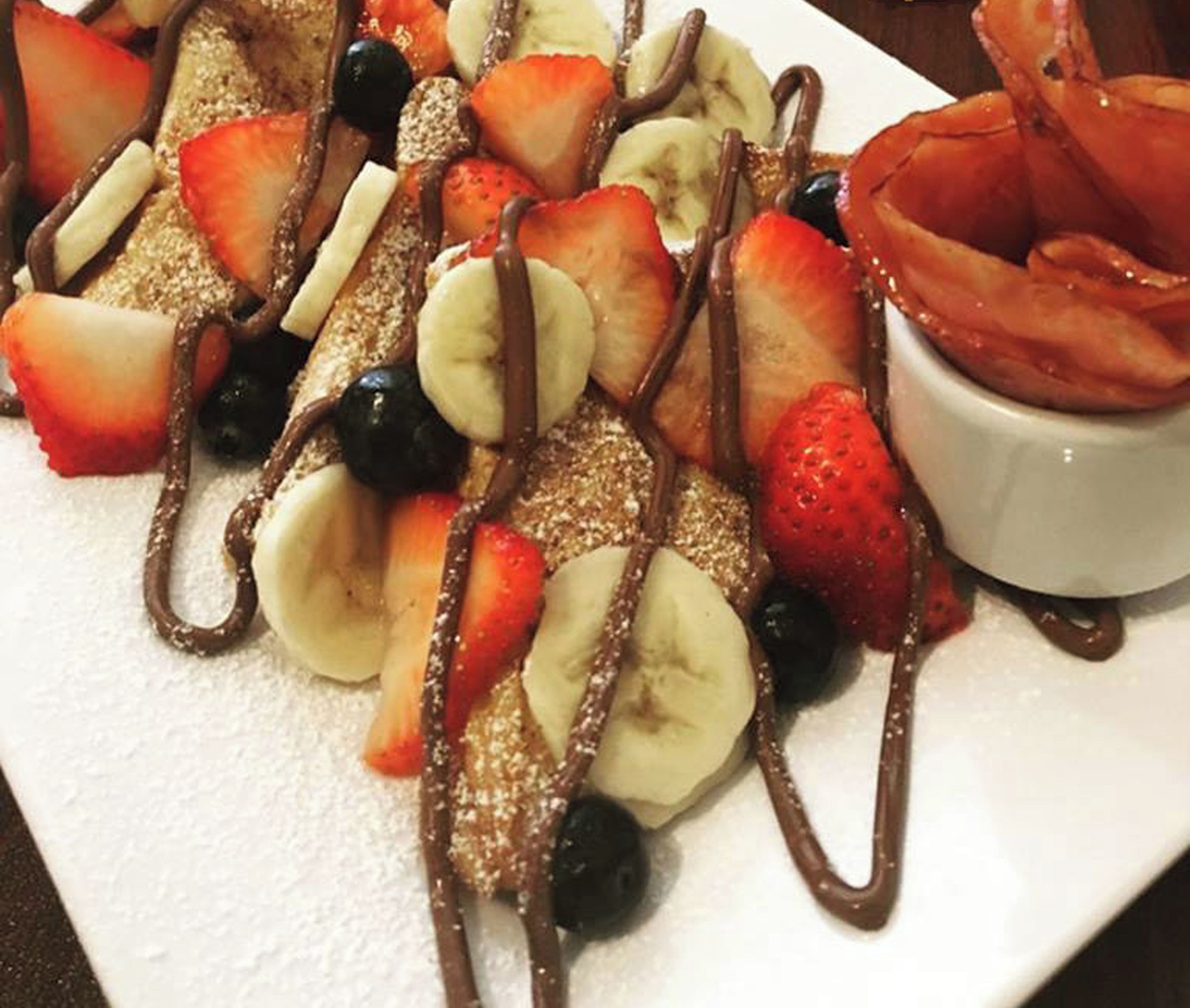 Une assiette de dessert avec des fraises, des bananes et une sauce au chocolat, ainsi qu’un bol de fraises.