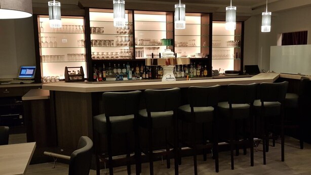 A bar area with a counter, multiple bar stools, and a shelf with various bottles and glasses. - Hotel Restaurant Teichaue (Adendorf)