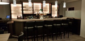 A bar area with a counter, multiple bar stools, and a shelf with various bottles and glasses.