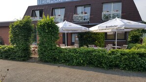 A building with outdoor seating and umbrellas, a brick facade, and a sign that reads "TEICHBAUER". - Hotel Restaurant Teichaue (Adendorf)