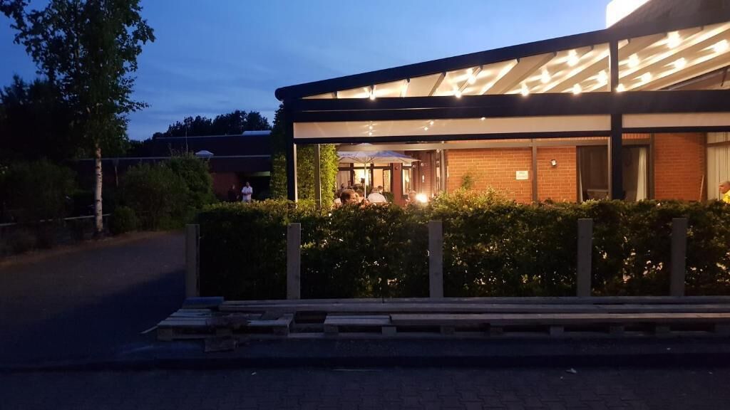 A modern building with a covered outdoor area, possibly a restaurant or cafe, with a brick facade and a glass enclosure.