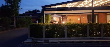 A modern building with a covered outdoor area, possibly a restaurant or cafe, with a brick facade and a glass enclosure.
