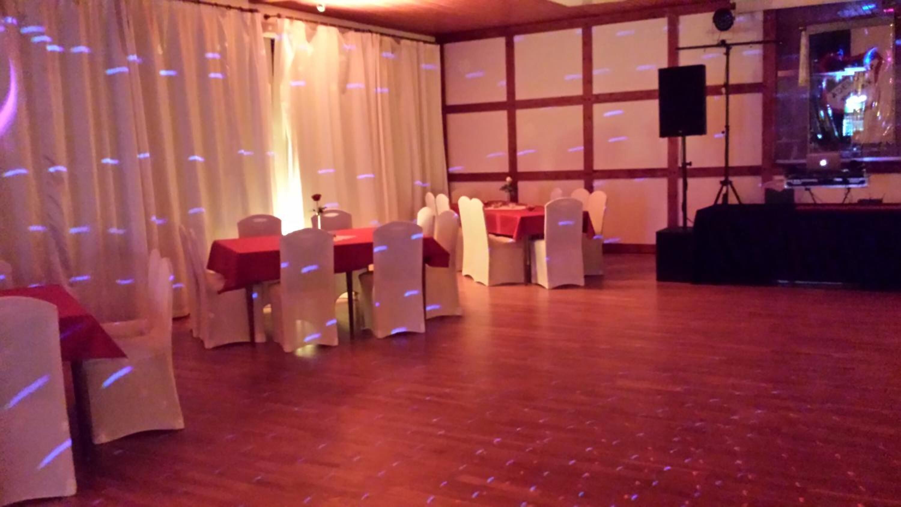 Un salón de banquetes con mesas dispuestas para comer, sillas blancas y un escenario con un orador.