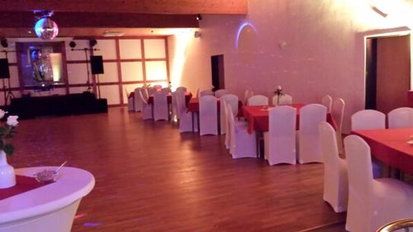 A banquet hall with tables set for events, white chairs, and a stage with a disco ball.