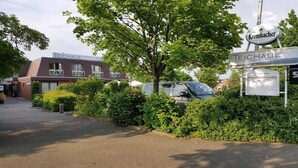A hotel named 'Teichaue' with a signboard, a parking area, and a tree in the foreground. - Hotel Restaurant Teichaue (Adendorf)