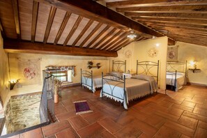 Una camera da letto rustica con travi in legno, tre letti in metallo, pareti in pietra e una scala in pietra.