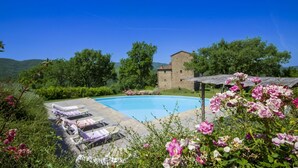 Ein Pool mit Liegestühlen, ein Steinhaus und üppiges Grün.