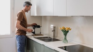 Eine Person bedient eine Kaffeemaschine in einer modernen Küche mit Spüle und einer Vase voller gelber Tulpen.