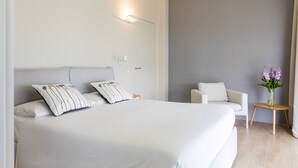 Ein modernes Hotelzimmer mit einem großen Bett, einer kleinen Couch, einem Nachttisch und einer Vase mit Blumen.